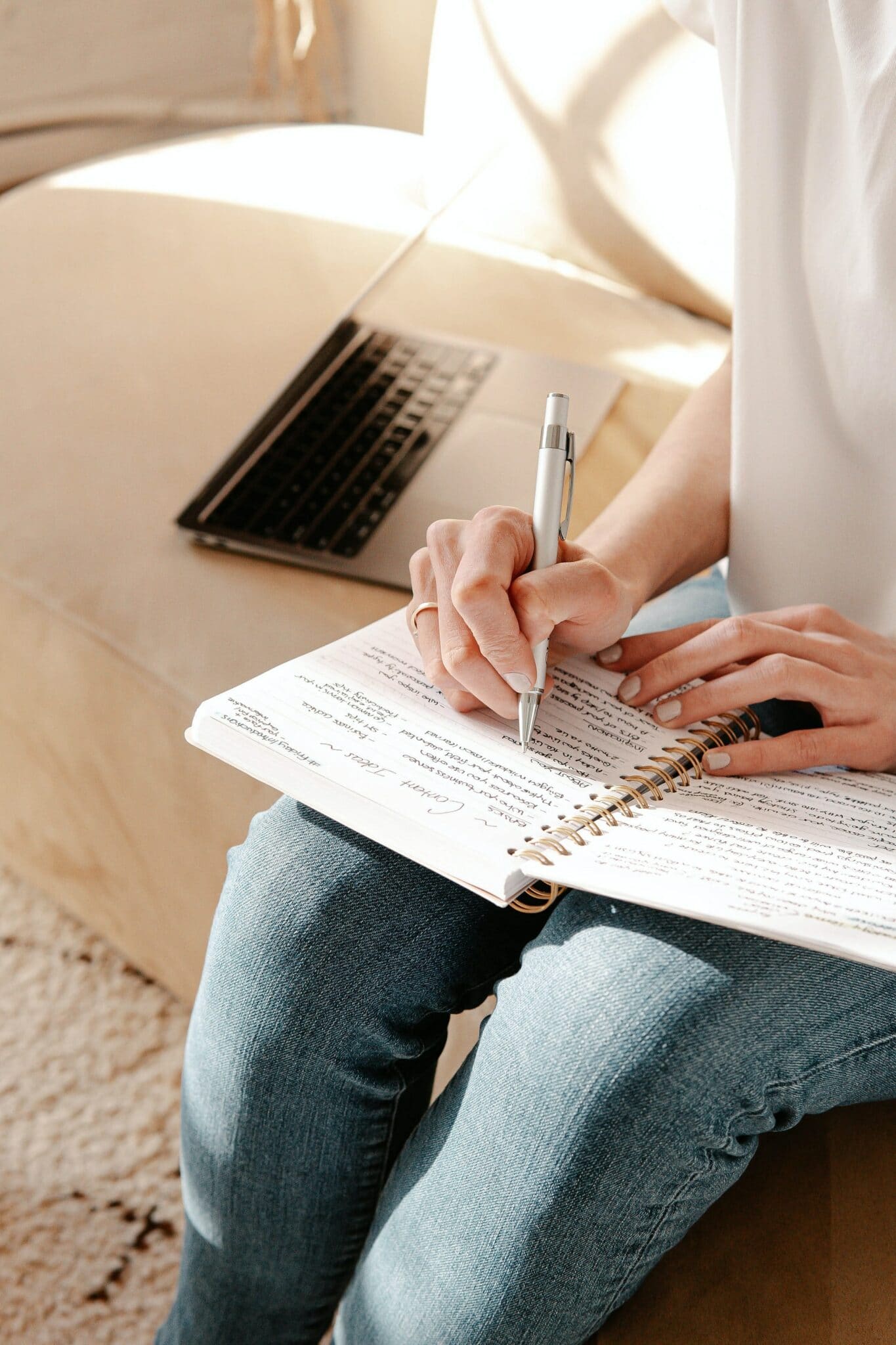 Woman sitting on side of bed, writing in a notebook
