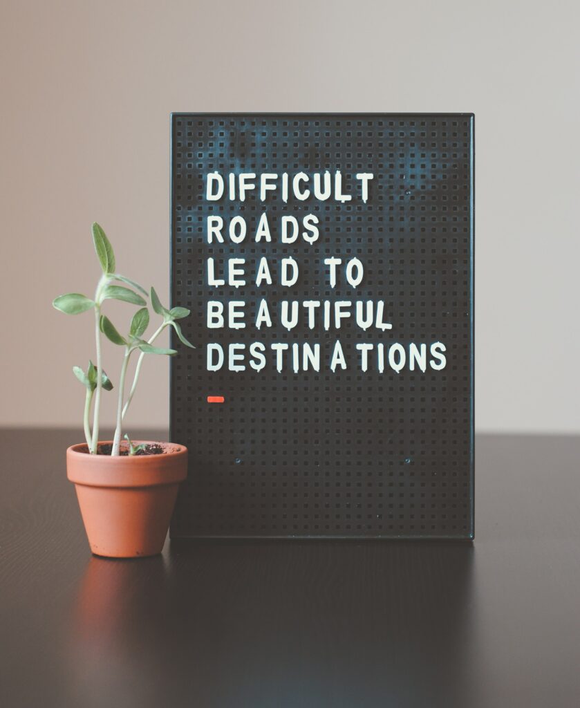 Sign that read "Difficult Roads Lead To Beautiful Destinations" on a desk next to plant
