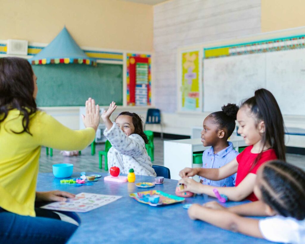 Teacher and kids in classroom, child giving teacher a high-five as they work on art project