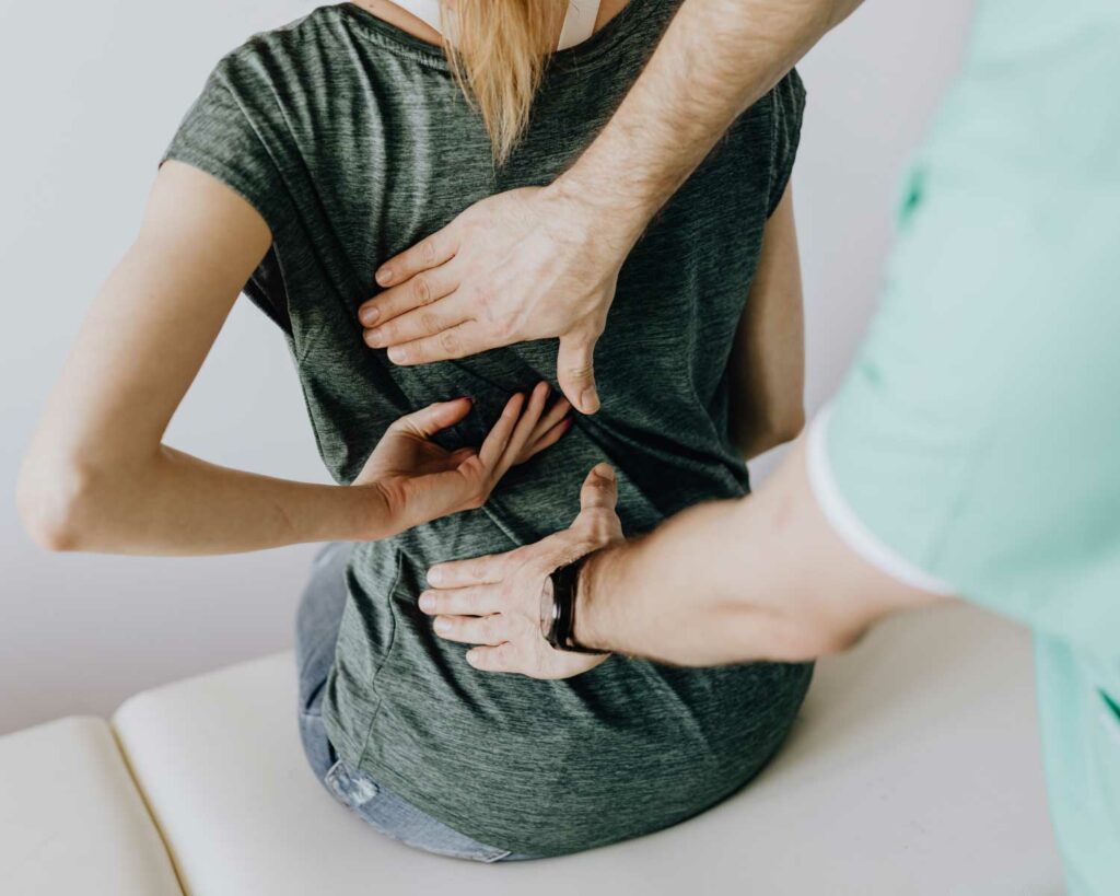 Woman sitting on doctor table with her back towards chiropractor while they align her back