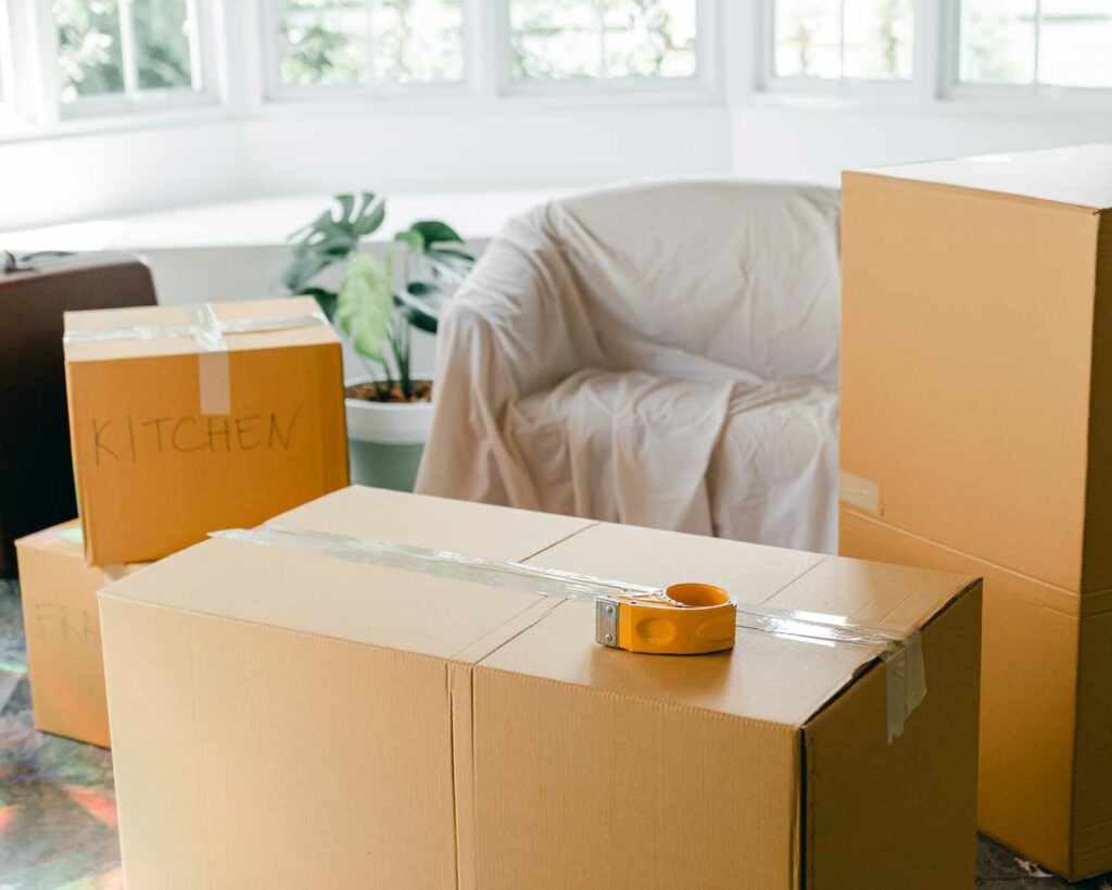 A living room with furniture covered with sheets and moving boxes with labels and tape around