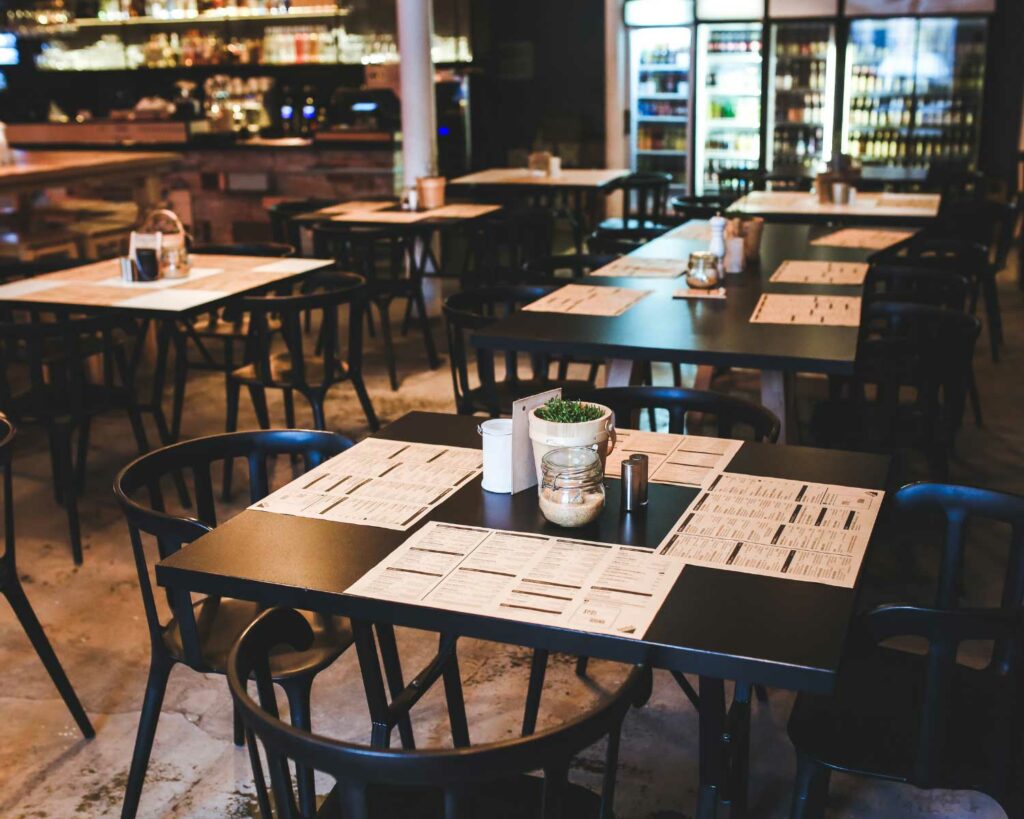 View of open restaurant with black tables and chairs and menus on tables